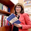 Portrait photo: Assoc. Prof. Eng. Magdalena Grębosz-Krawczyk, TUL Prof. is standing by a bookcase. She is holding one of the books open in her hands.