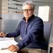 Portrait photo: Dr Eng. Jakub Szczepaniak is sitting sideways at a white desk. On the tabletop an open thick notebook and a computer screen.