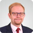 Zdjęcie portretowe: dr inż. Paweł Latosiński w niebieskiej marynarce, białej koszuli i krawacie na jasnym tle.