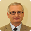 Zdjęcie portretowe: prof. Bogusław Więcek w jasnym garniturze i białej koszuli na kremowym tle.