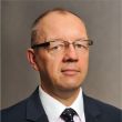 Zdjęcie portretowe: prof. dr hab. inż. Tomasz Kubiak w ciemnej marynarce, białej koszuli i krawacie na szarym tle.