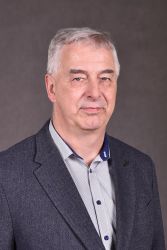 Zdjęcie portretowe: Piotr Urbanek na szarym tle.