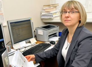 Zdjęcie portretowe: dr inż. Janina Leks-Stępień siedzi przy biurku. W tle dokumenty, komputer i drukarka.