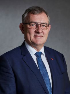 Portrait photo: Prof. Krzysztof Jóźwik in a navy blue suit, white shirt and a blue tie against grey background.