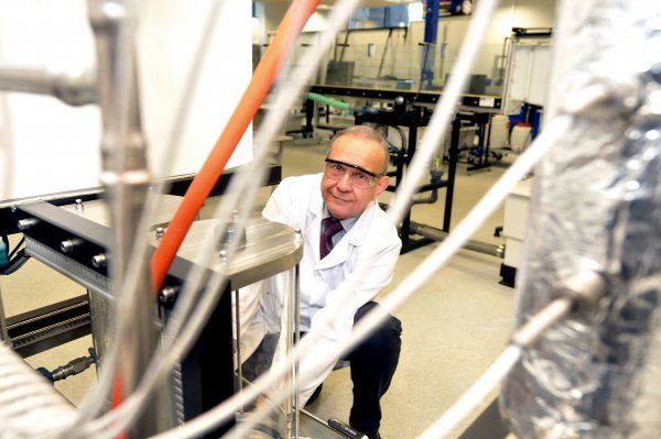 Portrait photo: Prof. Andrzej Górak, in a white lab coat and safety goggles, takes measurements in a specialised laboratory.