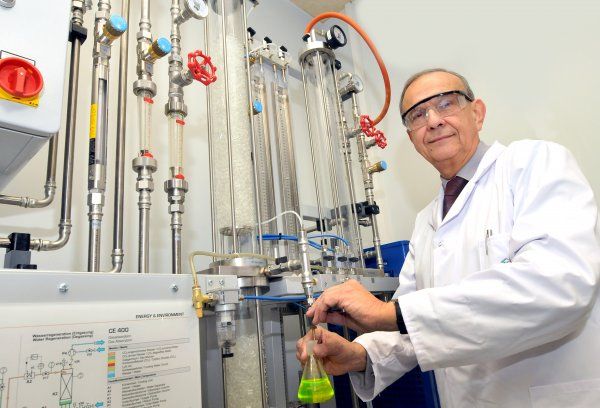 Portrait photo: Prof. Andrzej Górak, wearing a white lab coat and safety goggles, stands next to a specialised device.
