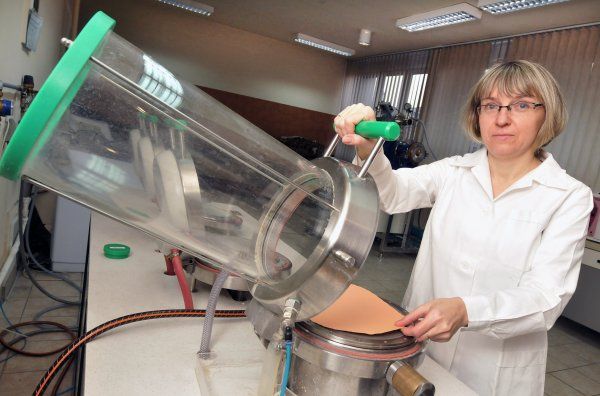 Zdjęcie portretowe: dr inż. Janina Leks-Stępień w białym fartuchu stoi lewym profilem przy specjalistycznym urządzeniu - przeźroczystej tubie