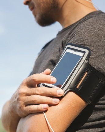 Left hand of a man in a grey t-shirt with a phone band attached to his arm.