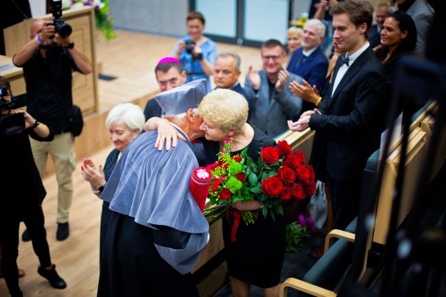 mężczyzna przekazujący koobiecie bukiet kwiatów, wokół widownia w auli
