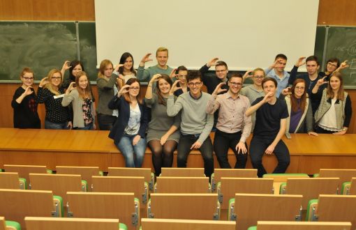 Zdjęcie portretowe: grupa ok 30 studentów z SKN Cirkula w sali wykładowej na katedrze. Prawe dłonie mają ułożone w literę C. Z tyłu biała i zielone, szkolne tablice.