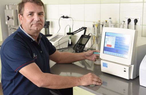 Zdjęcie portretowe: dr hab. inż. Piotr Dziugan w niebieskiej polówce przy stole laboratoryjnym na którym stoi urządzenie pomiarowe. 