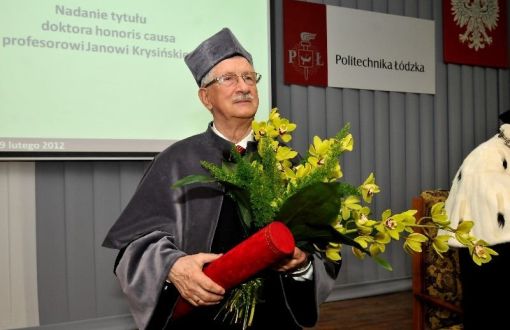 Portrait photo: Prof. Jan Krysiński in grey gown with flowers and a red tube at the ceremony of awarding the DHC of TUL.
