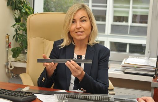 Zdjęcie portretowe. Uśmiechnięta prof. Renata Kotynia siedzi przy biurku w swoim gabinecie. W dłoniach trzyma metalowy element konstrukcji.