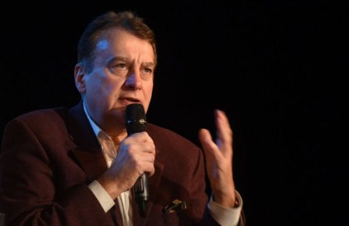 Paweł Sztompke w brązowej marynarce i jasnej koszuli siedzi i mówi do mikrofonu, który trzyma w prawej ręce.