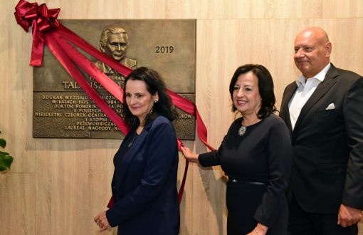 Przed ścianą z tablicą pamiątkową prof. T. Paryjczaka z czerwoną szarfą stoją dwie jego córki i syn.