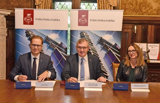 Dyrektor Jan Filocha, rektor prof. Krzysztof Jóźwik i kwestor PŁ Agnieszka Kobalczyk siedzą przy drewnianym stole. Przed nim umowy i pióra. W tle dwa roll upy uczelni.