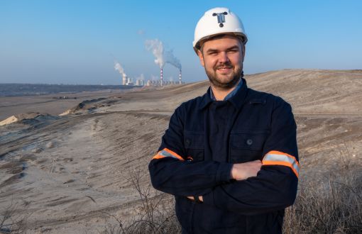 Damian Kądrowski w kasku na tle wykopalisk.