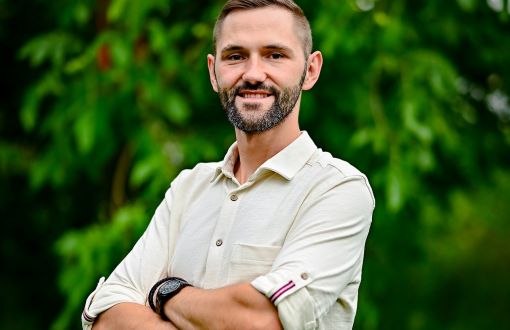 Zdjęcie portretowe: dr inż. Bartosz Sekuła na tle zieleni.