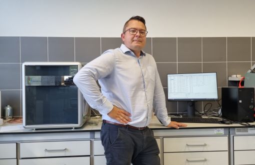 dr inż. Szymon Szufa stoi przy aparaturze badawczej.