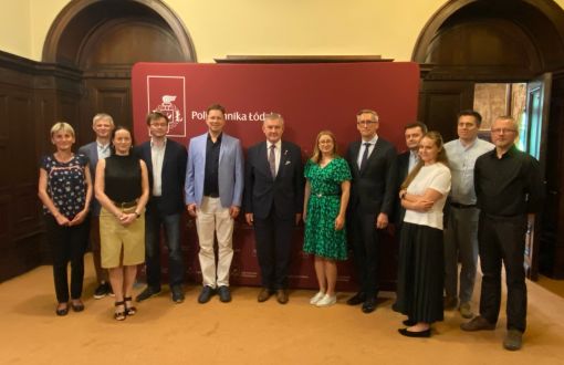 uczestnicy spotkania stoją w grupie na tle ścianki z logo Politechniki Łódzkiej, znajdują się w rektoracie PŁ