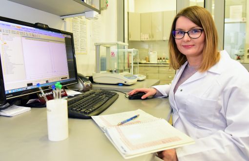 kobieta naukowiec siedzi przed komputerem w laboratirium ubrana w biały fartuch