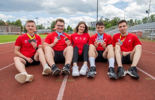 zdjęcie 5 sportowców siedzących na bieżni i pokazujących medale