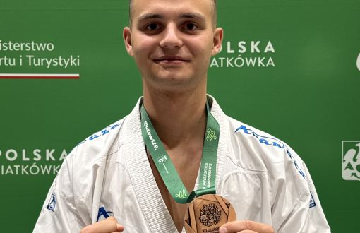 młody sportowiec pozuje z brązowym medalem na tle zielonej ścianki