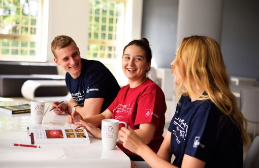 Młodzi, usmiechnięci ludzie w kolorowych podkoszulkach siedzą przy stole i rozmawiają